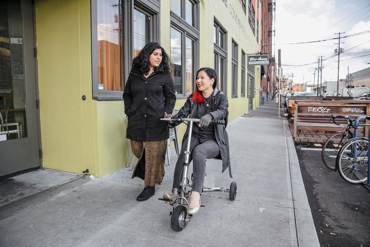 Two friends out on a city sidewalk, one riding a mobility scooter