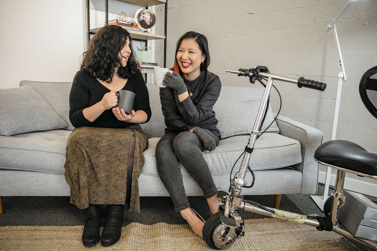 Two friends sharing coffee on a couch with a mobility scooter beside them